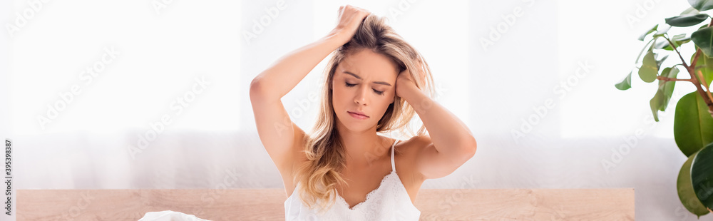 Naklejka premium woman with hands near head suffering from headache in bedroom, banner