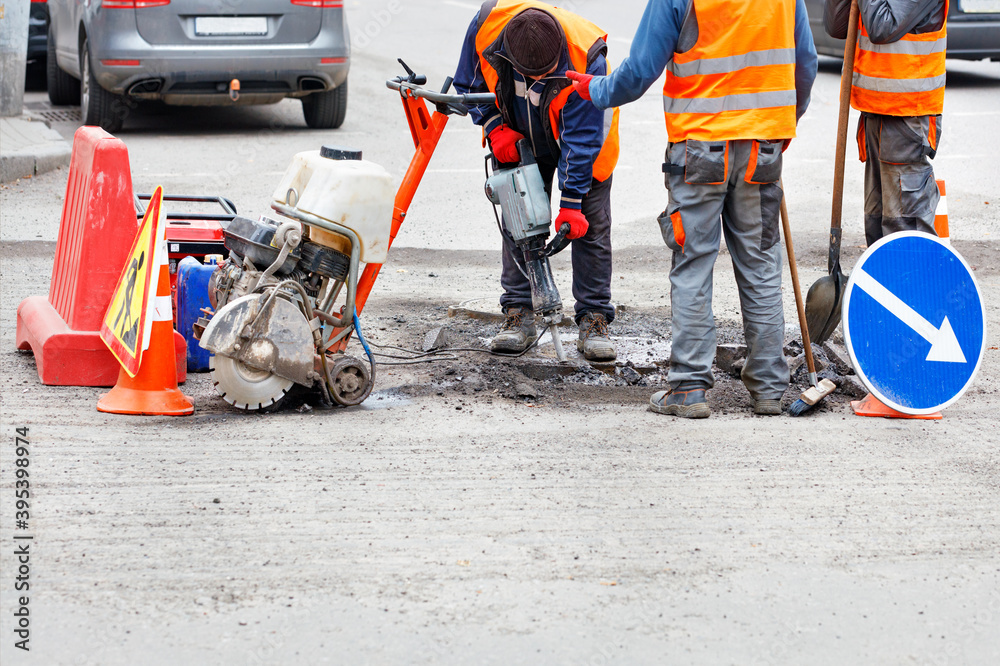 A team of road workers with hand-held road tools are repairing a section of the road.