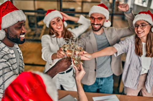 Merry Christmas and Happy New Year! Multiracial young creative people are celebrating holiday in modern office. Group of young business people are drinking champagne in coworking.