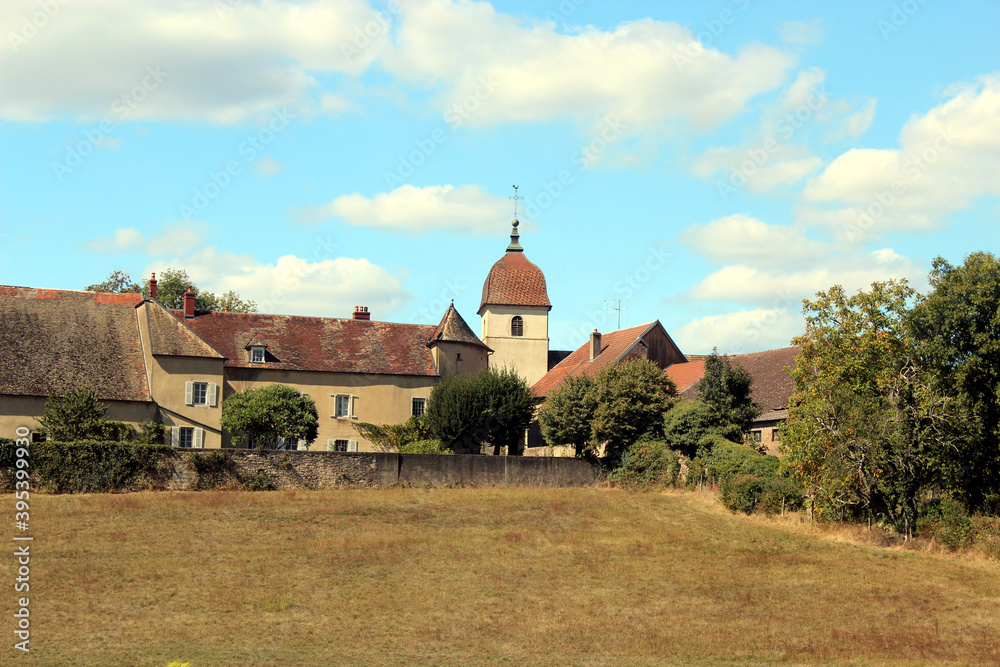 French village with beautiful houses, tall church and a green agricultural field.