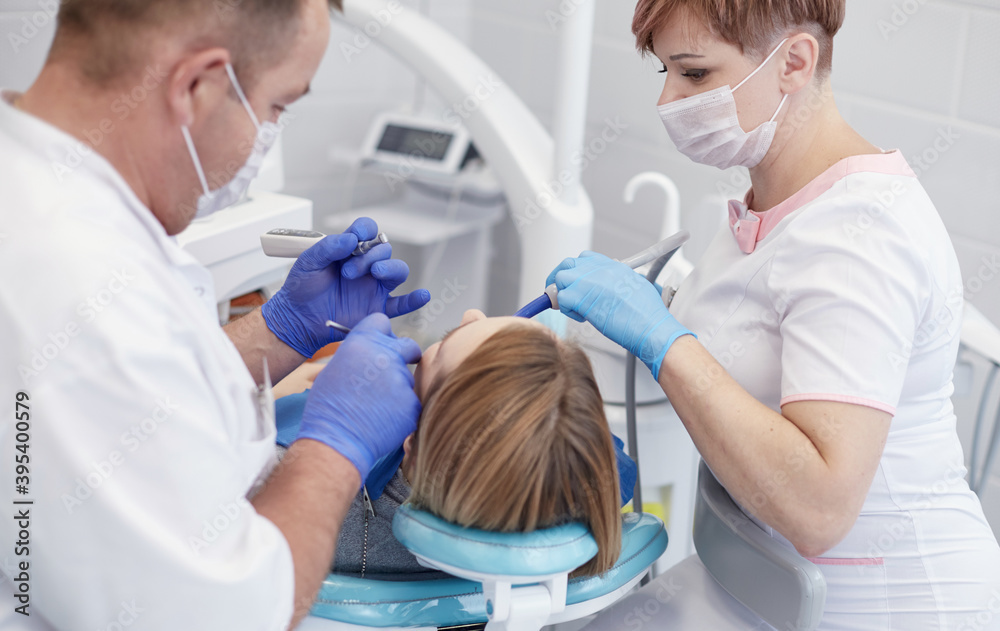 Fototapeta premium Doctor dentist treats teeth of a beautiful young girl patient. The girl on reception at the dentist. Doctor dentist treats tooth