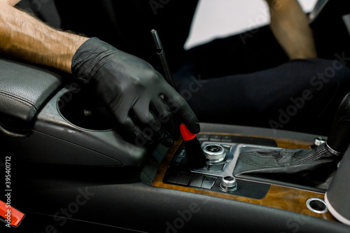 Cropped close up image of hand of male car service worker in rubber glove, cleaning dust from interior of luxury car, using special soft brush. Car cleaning and detailing concept, dry wash