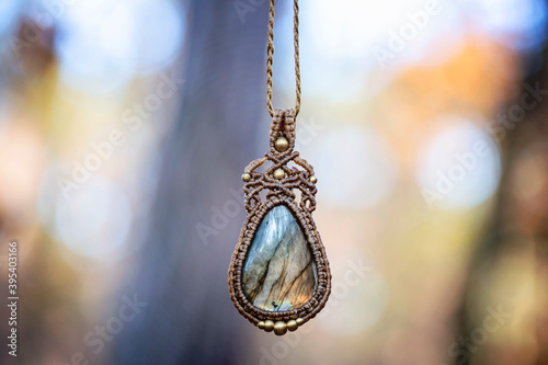 Mineral labradorite gemstone ornamental pendant on blury forest background