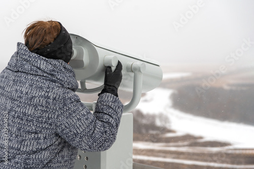 A woman looks through a binoscope at a winter landscape. Copy space. photo