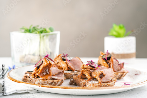 Open sandwiches on rye bread with pickled mushrooms chanterelles and ham on a white plate