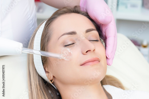 Cosmetologist performs a pulse current procedure for the face of a young woman.