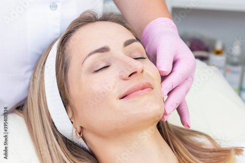 Cosmetological facial massage. beautician doing facial massage to a satisfied beautiful young woman