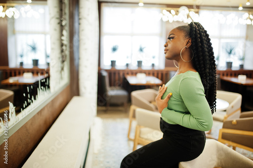 Portrait of attractive young african american woman wearing in green sweater and black jeans pose against mirror.