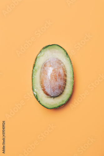 Avocado in wrap polyethylene plastic on colored background. Minimal enviromental concept. Flat flat, top view