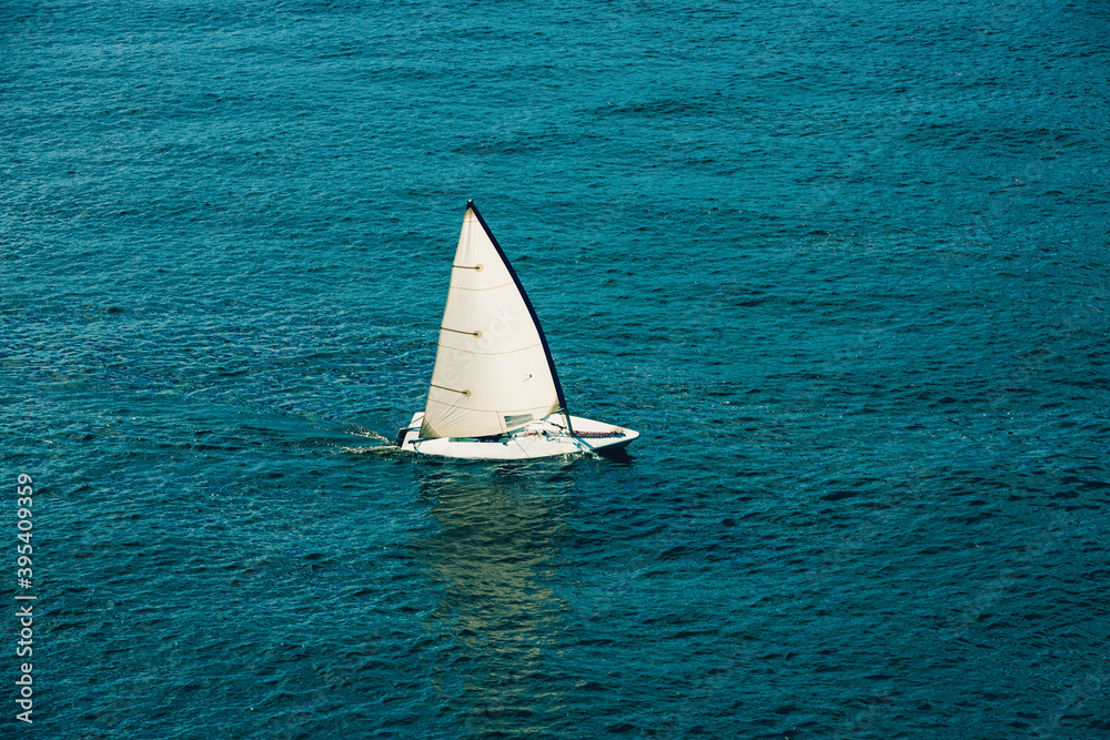 Sailing boat in open sea at sunlight. White sail on blue water. Luxury yacht in the ocean. Aerial view of Regatta sailing