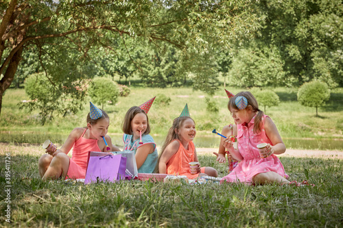 Girls celebrate their birthday in nature in party hats. Green trees in the background.