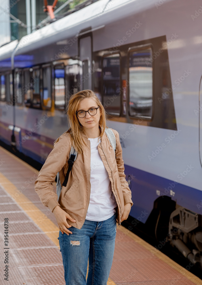 Fototapeta premium Young woman on the platform waiting for the train. Beautiful girl at the train station. Travel by train. Railway station in Bydgoszcz. Poland.