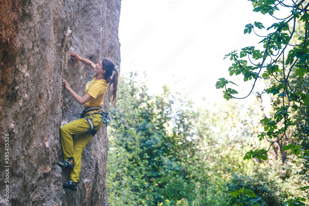 A strong woman climbs a rock on the background of the forest.