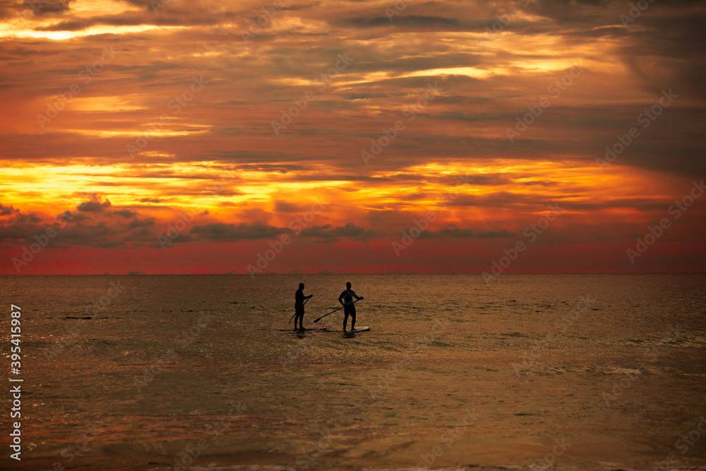 Sea sup surfing under amazing dark sunset sky. Two people on Stand Up Paddle Board. Orange sky. Paddleboarding Concept. Phuket. Thailand.