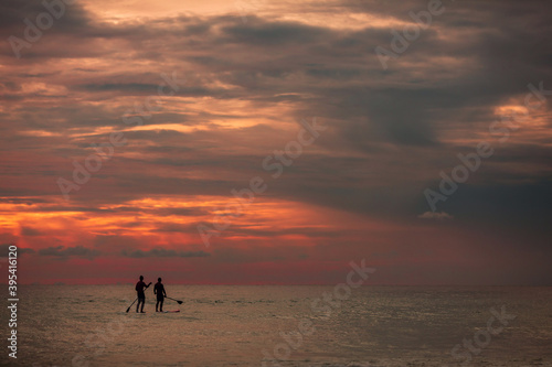 Sea sup surfing under amazing dark sunset sky. Two people on Stand Up Paddle Board. Orange sky. Paddleboarding Concept. Phuket. Thailand.