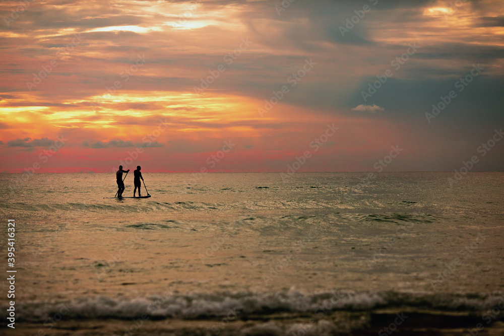 Sea sup surfing under amazing dark sunset sky. Two people on Stand Up Paddle Board. Orange sky. Paddleboarding Concept. trips to warm destinations.  Phuket. Thailand.