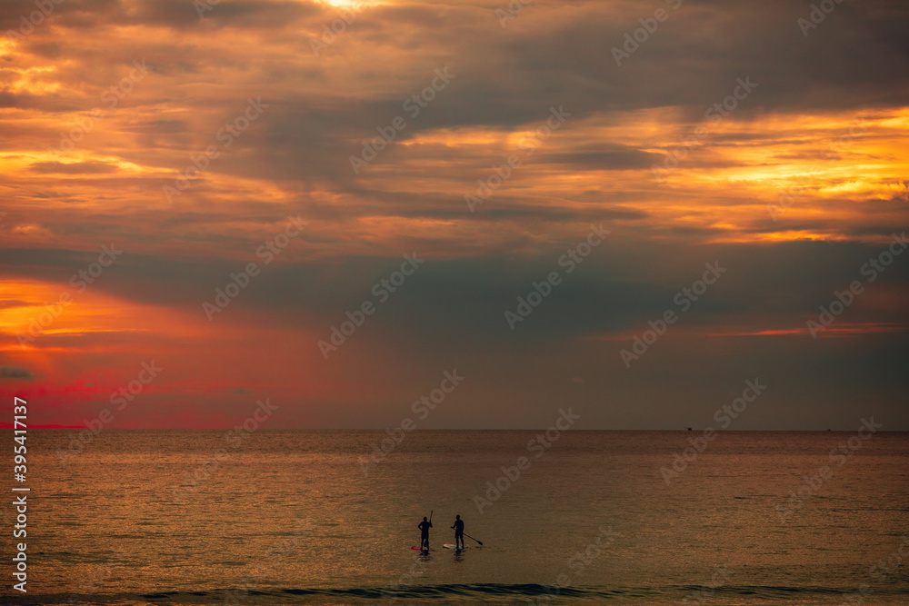 Sea sup surfing under amazing dark sunset sky. Two people on Stand Up Paddle Board. Orange sky. Paddleboarding Concept. trips to warm destinations.  Phuket. Thailand.