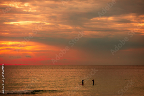 Sea sup surfing under amazing dark sunset sky. Two people on Stand Up Paddle Board. Orange sky. Paddleboarding Concept. trips to warm destinations. Phuket. Thailand.
