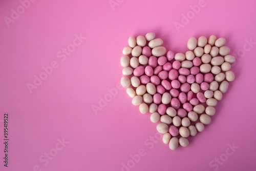 White and pink candies in glaze and with peanuts inside are laid out in the shape of a heart on a pink background. Copy space. February 14, Valentine's Day concept