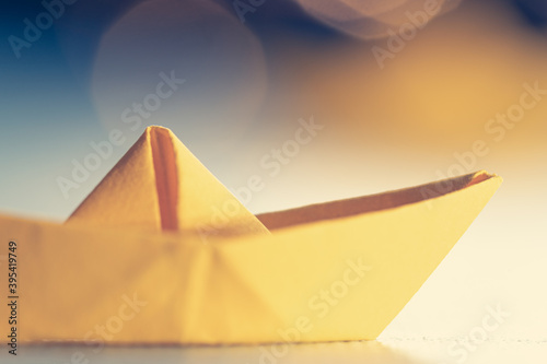Origami yellow sailing boat on a sea made with blue paper. Paper art style background with ship  ocean and bokeh lights
