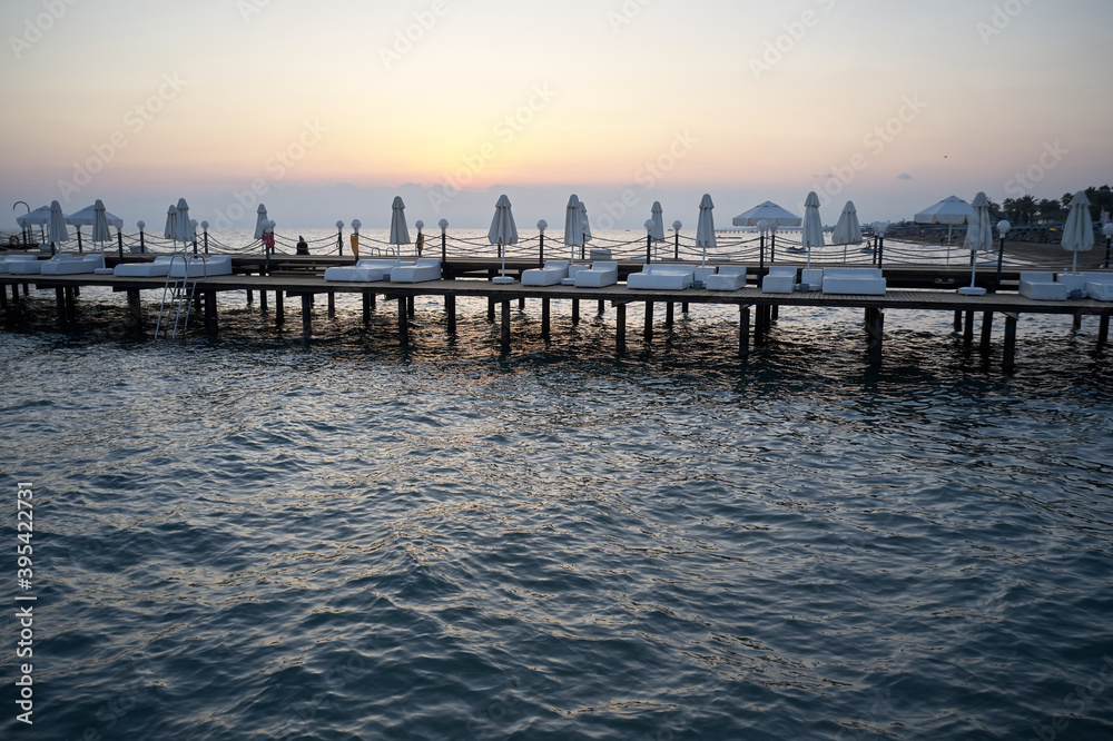 Obraz premium Wooden pier with empty sunbeds in the sea. Wavy sea with long wooden bridge at sunset sky background. Vacation at exotic country.