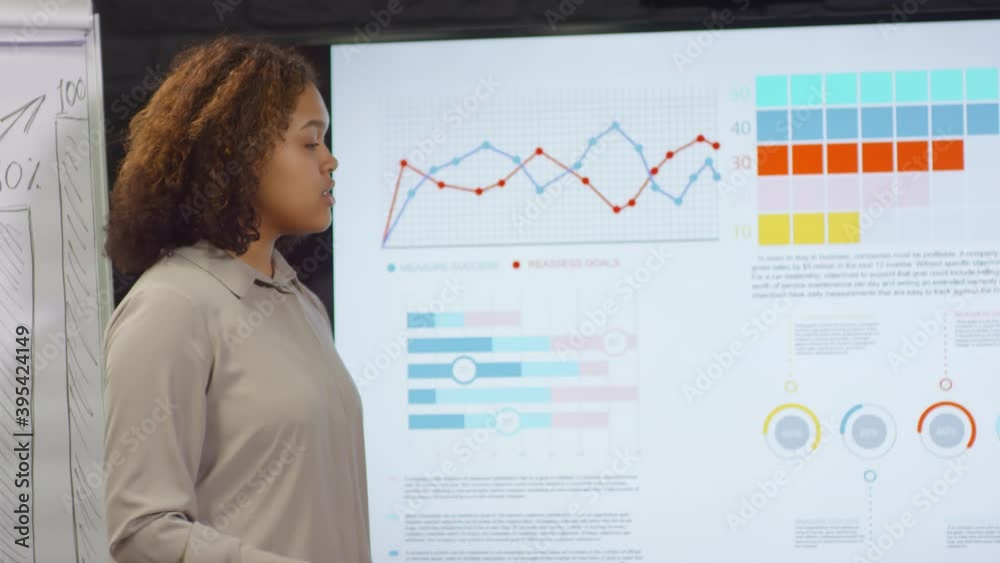 Medium close up of cheerful mixed race woman making presentation of company sales to coworkers looking at camera smiling Medium close up of cheerful mixed race woman making presentation of company sales to coworkers looking at camera smiling