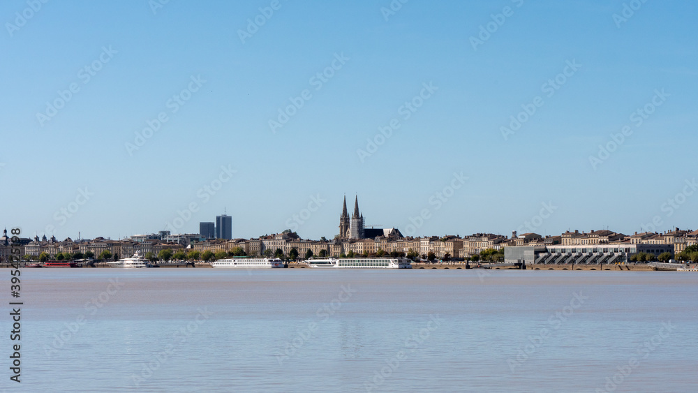 View on the Garonne river and city river bank in Bordeaux, a city located in southwestern France. In the background we can see the towers of the cathedral. Sunny day, blue sky.