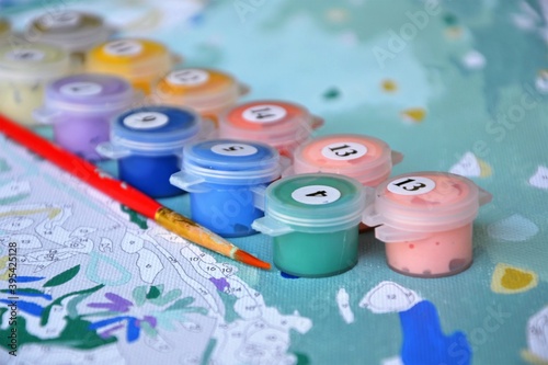 Painting by numbers, creative hobby. Small jars filled with paint on a painted canvas. Creative hobby, DIY. Set to paint the picture with canvas, paints in different colors, brushes. Selective focus