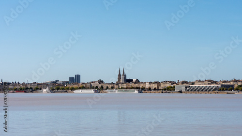 View on the Garonne river and city river bank in Bordeaux, a city located in southwestern France. In the background we can see the towers of the cathedral. Sunny day, blue sky. © Adrien