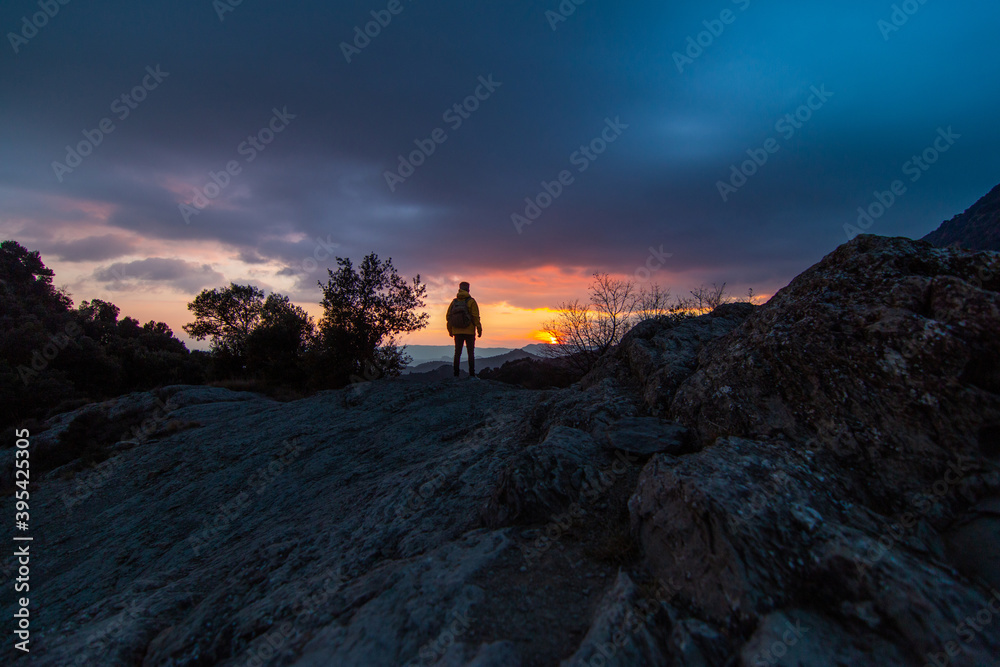 Young traveler man observing the sun on a beautiful sunset or sunrise. Rear view of adventurer backpacker in the nature, mountain. Concept of traveling with space for text, copy space.