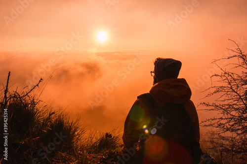 Backpacker observing the sun on a beautiful sunset or sunrise. Rear view of traveler young man. Concept of traveling and adventure.