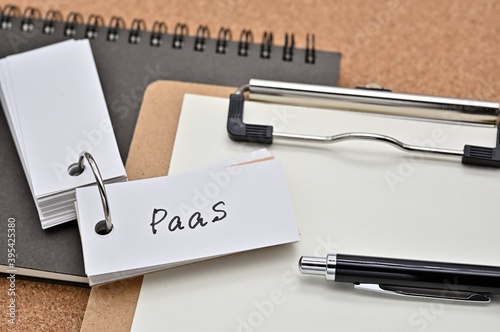 On top of the notebook and clipboard is a wordbook and pen with the word PaaS written on it. It means Platform as a Service. photo