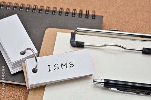 On top of the notebook and clipboard is a wordbook and pen with the word ISMS written on it. It means Information Security Management System. photo