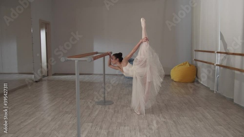 Gorgeous ballerina shows amazing ballet poses at barre in the dance hall photo