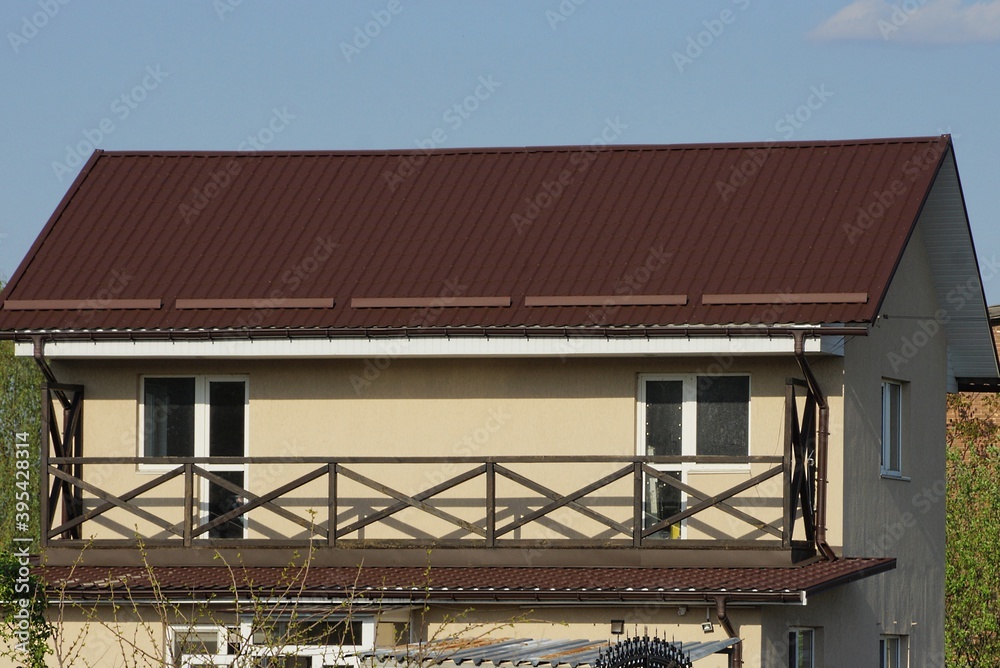 open long brown wooden balcony on the wall of a private house under a tiled roof against a blue sky on a sunny day