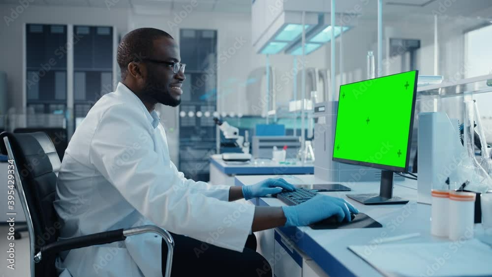 Modern Medical Research Laboratory: Scientist working on Computer Showing Green Chroma Key Screen. Scientific Lab, Medicine Development Facility with Advanced Equipment, Biotechnology. Side View Shot Modern Medical Research Laboratory: Scientist working on Computer Showing Green Chroma Key Screen. Scientific Lab, Medicine Development Facility with Advanced Equipment, Biotechnology. Side View Shot