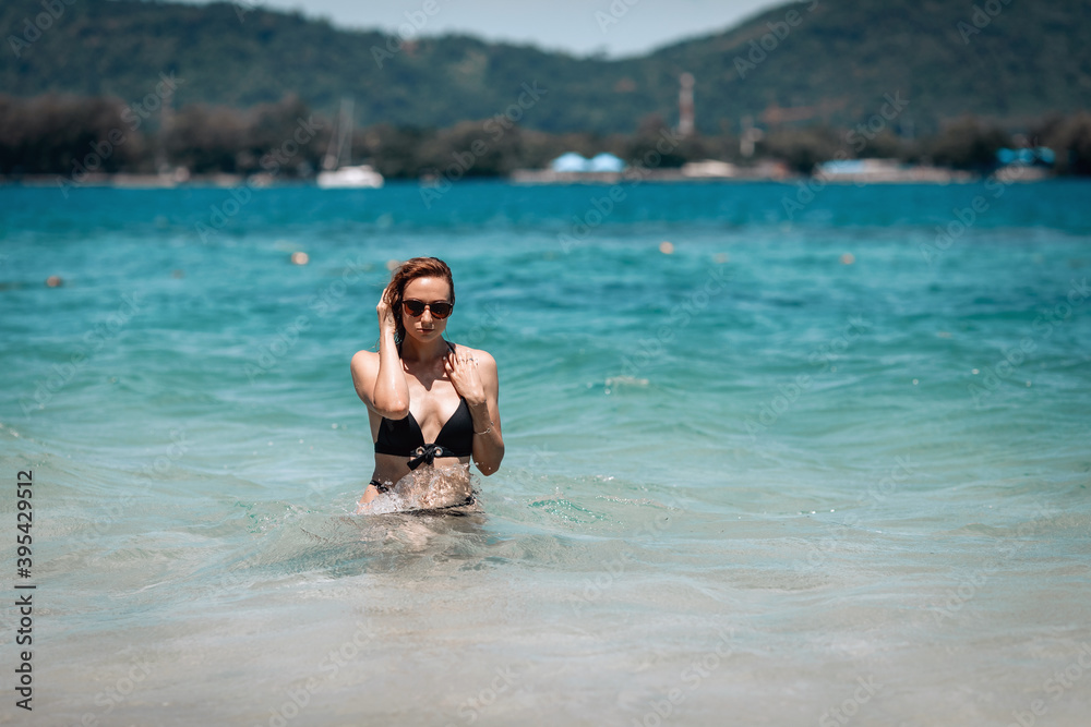A young beautiful girl in black sunglasses and black bikini staying in blue water in the sea ,enjoying beach holiday