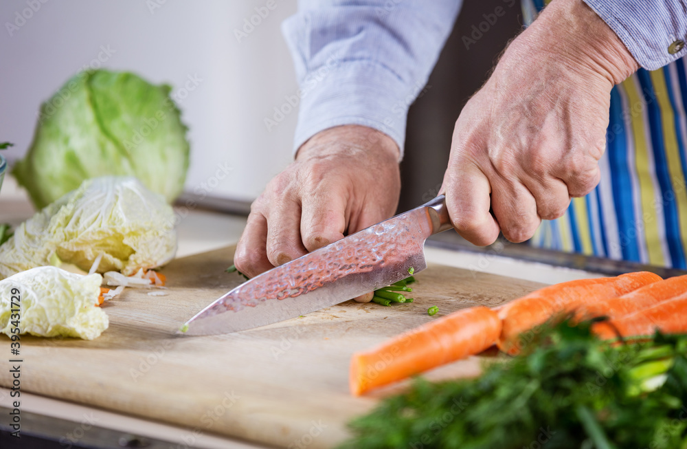 Cropped view of mature man chopping fresh vegetables for salad. Closeup of male hands.