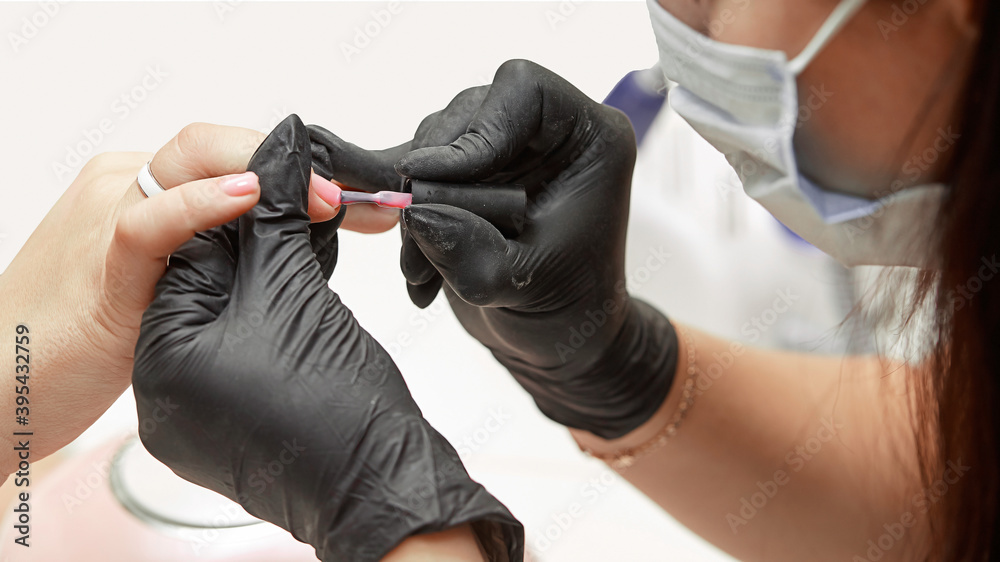 The manicurist applies a base coat to the nails. Close-up of the process of covering the nails with transparent varnish, manicure base, nail care, black gloves, cleanliness and care in the salon
