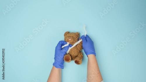 funny vintage brown curly teddy bear with rewound paw with white gauze bandage on blue background, concept of injuries in children or animals, top view