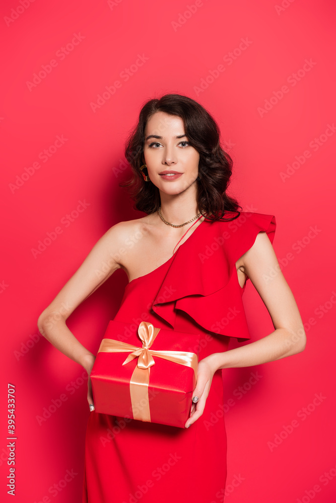 woman smiling while holding gift on red background woman smiling while holding gift on red background