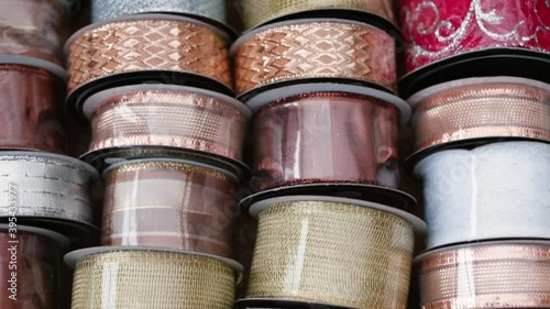Close-up of a variety of ribbons for decorating gifts and interiors before the holidays. The silvery and golden colors lend a shiny texture. Hand picks up one of the rolls of haberdashery tape.