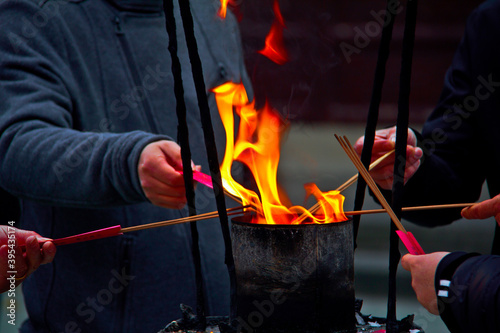 Closeup of four people lighting incense sticks from a large bright flame in a Chinese Buddhist temple