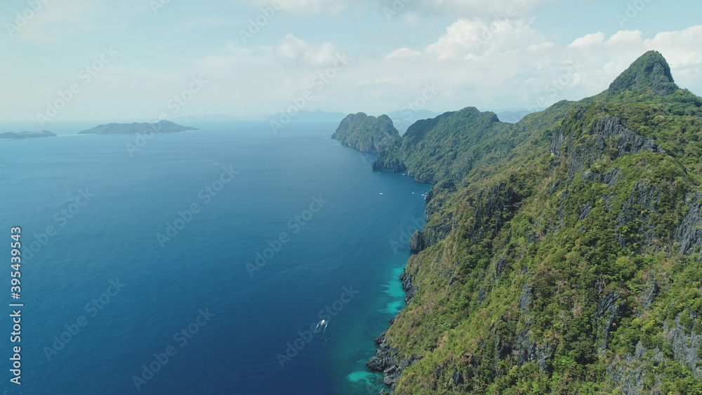 Aerial view of mountain island with green tropic forest. Epic landscape of ocean bay greenery cliff shore at sand beach. Boats at sea gulf with turquoise seascape of Palawan Island, Philippines, Asia