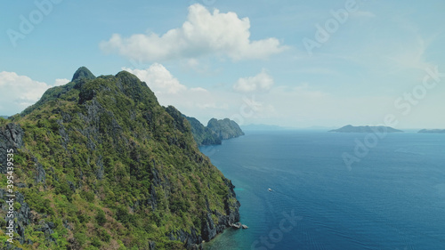 Mountainous island landscape with green tropic jungle forest. Majestic seascape of ocean bay greenery rocky shore at sand beach. Boats at sea waterfront of Palawan Island, Philippines, Asia drone shot