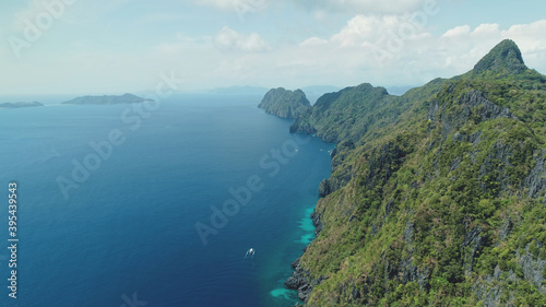 Aerial view of mountain island with green tropic forest. Epic landscape of ocean bay greenery cliff shore at sand beach. Boats at sea gulf with turquoise seascape of Palawan Island, Philippines, Asia