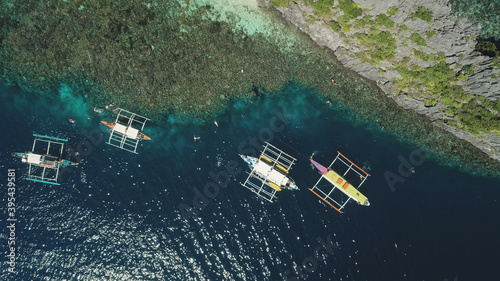 Top down aerial view of boats at cliff ocean shore, sand beach. Nature beauty of tropic mountain isle Palawan, El Nido Islands, Philippines, Asia. Epic summer landscape with vessels at rock coast