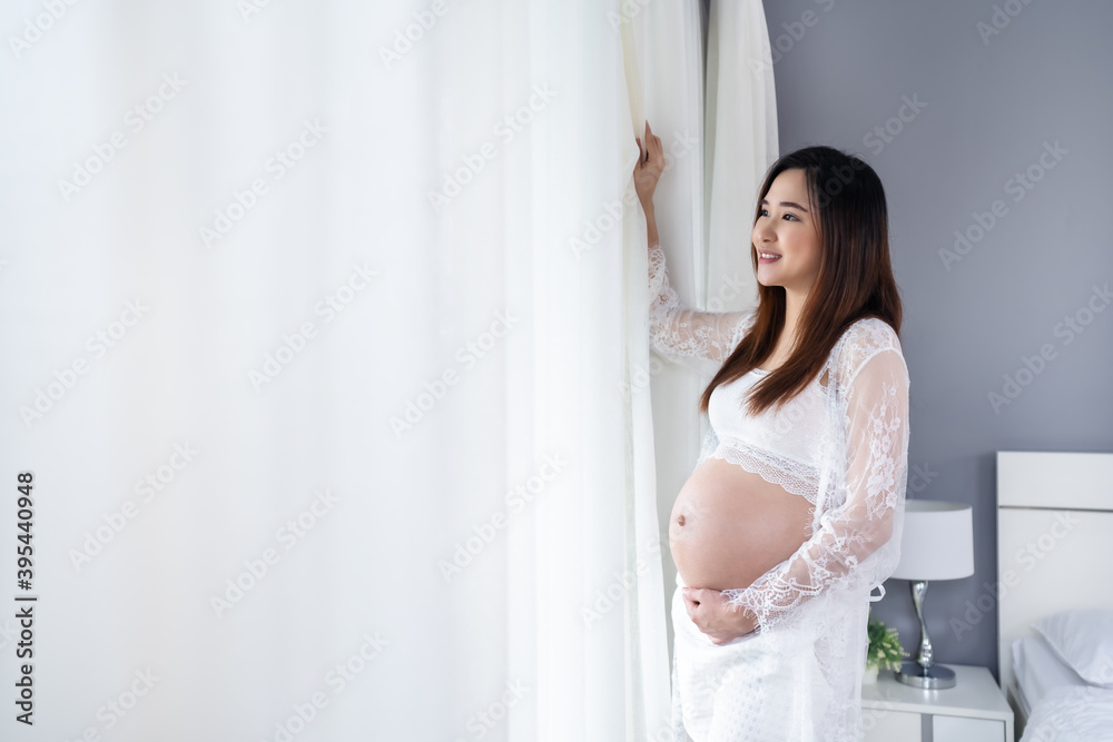 pregnant woman looking view at window and stroking her belly in the bedroom pregnant woman looking view at window and stroking her belly in the bedroom