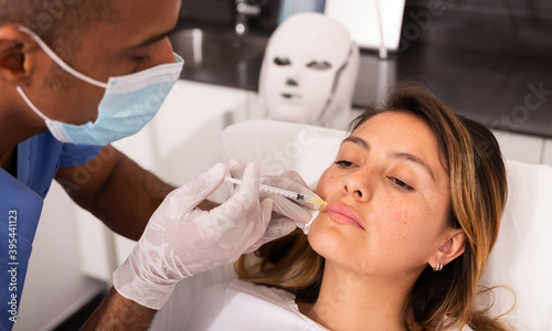 Young Hispanic woman getting procedure of injection contouring for facial correction in aesthetic cosmetology clinic