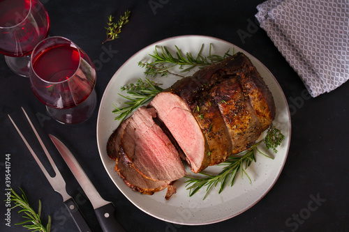 Roasted beef with herbs and red wine on dark background. View from above, top studio shot photo